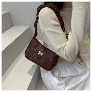 Détail du sac à bandoulière tressé bordeaux avec papillon argenté et bandoulière froncée