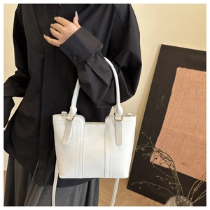 Detail of a white trapezoidal PU leather bucket bag with gold-tone hardware and top handles