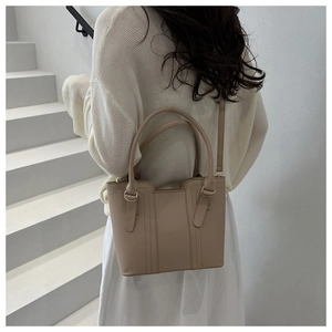 Model view of a beige minimalist tote bag with top handles and an adjustable shoulder strap