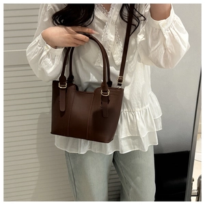 Detail of the minimalist dark brown leather bucket bag showing its matte texture and golden hardware
