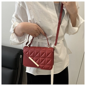 Detail of red quilted faux leather handbag with a gold metal bar on the front flap