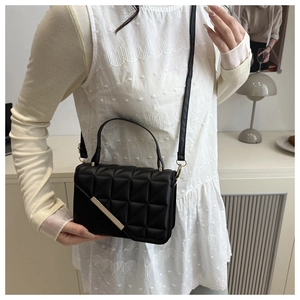 Close-up of black quilted shoulder bag with geometric patterns and gold metal bar detail