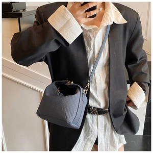 Blue mini crossbody bag with woven texture worn by model in professional black suit