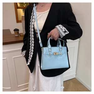 Light blue faux leather handbag with gold metal twist lock shown in a cafe setting