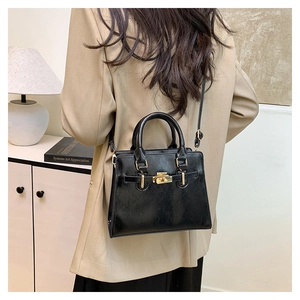 Chic black faux leather handbag with gold clasp and top handle shown on a model