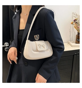Detail shot of a cream underarm bag featuring a metallic gold bow clasp on synthetic leather