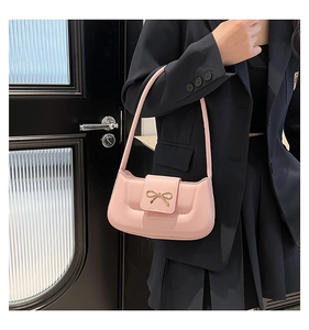 Détail du sac sous le bras en cuir rose avec un ornement de nœud doré délicat