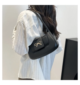 Détail d'un sac sous le bras en cuir noir avec une boucle dorée en forme de nœud sur la sangle