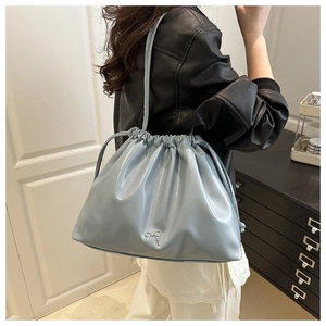 Detail of light blue glossy bucket bag with silver bow charm worn by a stylish model