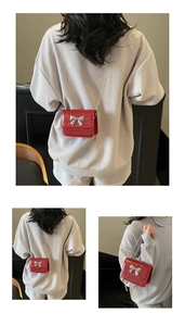 Detailed view of mini red crossbody bag with silver bow accent and slim chain strap