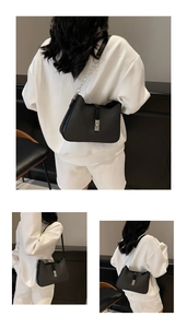 Detail of a black leather underarm bag featuring a silver metal chain and vertical buckle