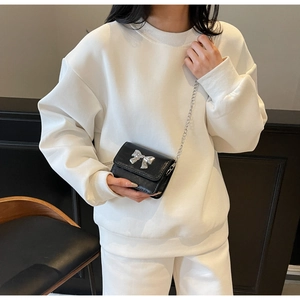 Detail of a black mini crossbody bag with a silver metal bow on a white sweatshirt
