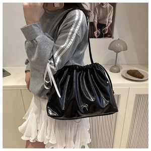 Close-up of black glossy drawstring bucket bag featuring a silver bow metal accessory