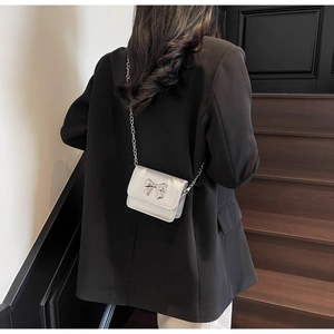 Silver mini crossbody bag with metal bow detail worn over a black blazer on a model