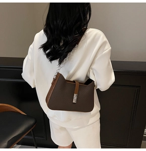 Detalle de bolso de hombro trenzado marrón oscuro con cadena y hebilla metálica en modelo