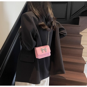 Detail of pink mini crossbody bag with silver bow accent on model in black blazer