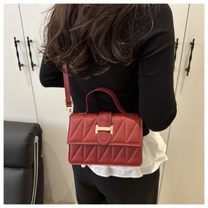 Detailed view of burgundy quilted crossbody bag with golden H-clasp on a female model