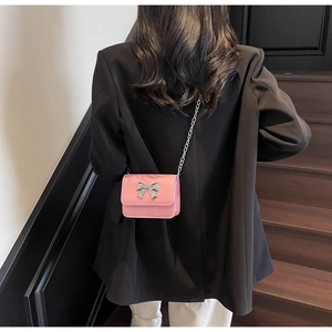 Close-up of pink crossbody bag with silver bow ornament worn by a model in black blazer