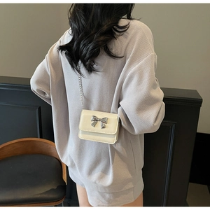 Rear view of a model wearing a mini cream crossbody bag with a silver metal bow