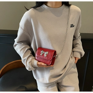 Red mini crossbody bag with silver bow detail and chain strap shown on a model