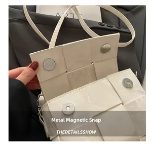 Detail of silver magnetic buckle and woven leather texture on cream crossbody bag