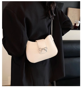 Detail of cream-white shoulder bag with silver bow accent on smooth leather-like texture