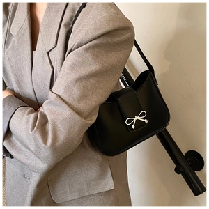 Detail of black leather underarm bag featuring a metallic silver bow on the flap