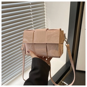 Detail of light pink woven crossbody bag featuring glossy patent leather finish and strap