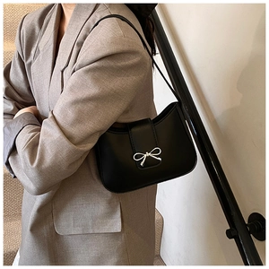Detail of black faux leather baguette bag featuring a silver metal bow buckle on shoulder strap