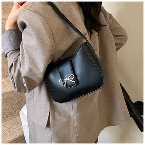 Close-up of black leather baguette bag with silver bow buckle on model's shoulder