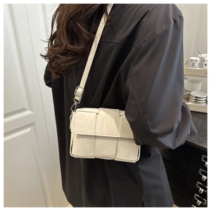 Detail of white woven crossbody bag showing textured leather and silver metal buckles