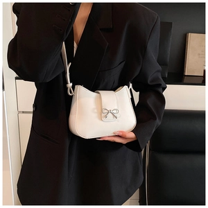Close-up of white leather underarm bag featuring a silver metal bow buckle detail