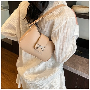 Chic beige underarm bag with silver bow detail shown worn by a model in a cozy setting