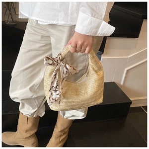 Détail du sac demi-lune en paille tressée avec foulard en soie sur l'escalier