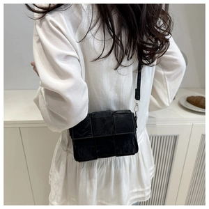 Model wearing a black woven crossbody bag featuring a classic wide-grid texture and leather strap