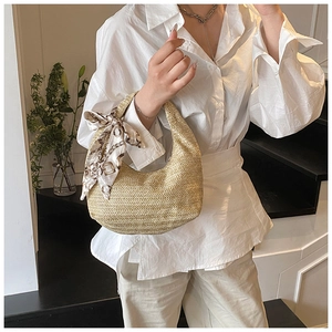 Détail du sac demi-lune en paille tressée avec un foulard en soie imprimé sur l'anse