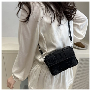 Close-up of black woven leather texture and silver hardware on a women's crossbody bag