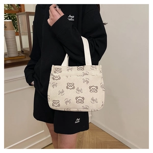 Detail view of corduroy tote bag featuring cartoon bear embroidery and front zipper pocket