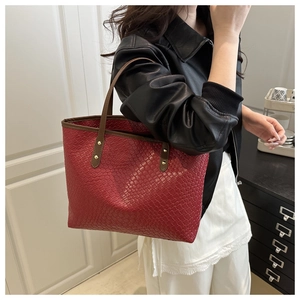 Detail of red woven tote bag featuring gold studs and brown leather handles on a model