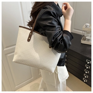 Close-up of white woven tote bag featuring deep brown leather handles and gold rivet details