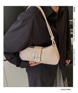 Detail of cream baguette bag with silver metallic logo buckle and knotted shoulder strap