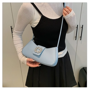 Close-up of light blue leather baguette bag with sparkling rhinestone buckle on shoulder