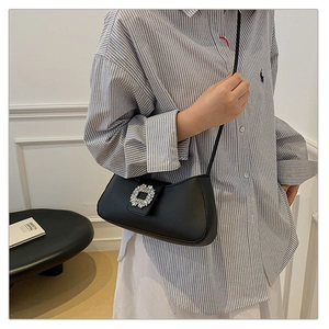 Detail of elegant black matte leather baguette bag featuring a large square crystal buckle