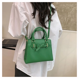 Détail du sac à main en cuir vert avec nœud et ferrures dorées sur chemise blanche