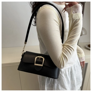 Close-up of elegant black leather shoulder bag featuring a large gold square buckle detail