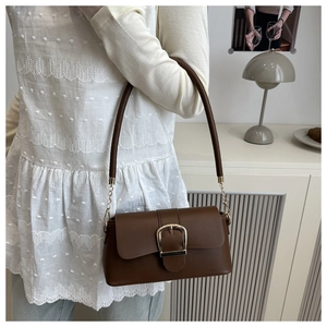 Brown matte leather shoulder bag with gold square buckle shown in a lifestyle home setting
