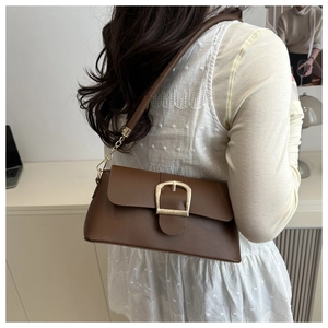 Dettaglio di una borsa a spalla marrone con grande fibbia dorata e tracolla in pelle e catena