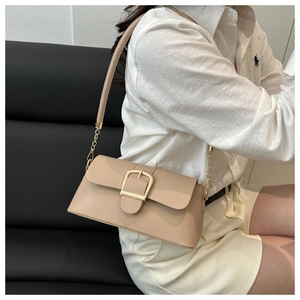 Detail of nude baguette bag with golden buckle on chain strap worn by a model