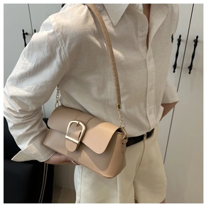 Detail of a cream faux leather shoulder bag with a large gold buckle on a crossbody strap