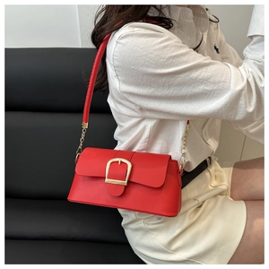 Close-up of vibrant red baguette bag with large gold buckle and leather chain strap